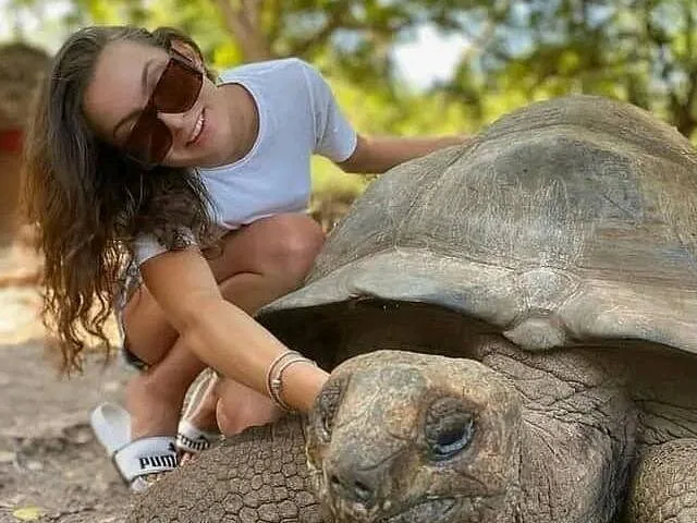 Eine Frau hockt neben einer Riesenschildkröte und berührt ihren Kopf.