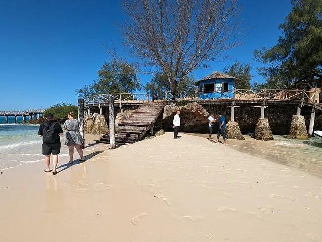 Touristen stehen an einem Sandstrand in der Nähe von Holzkonstruktionen.